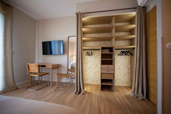 Habitación de hotel con escritorio de madera, una silla, televisión instalada en la pared, armario con estantes y una cama.