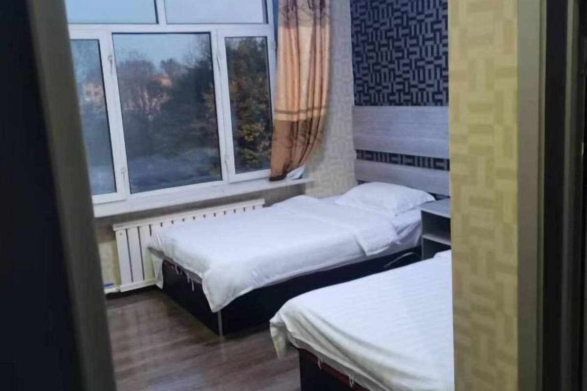 Una habitación con dos camas, una ventana con cortinas y un papel tapiz estampado.