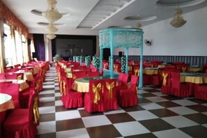 Un salón de banquetes con suelo a cuadros, mesas con manteles rojos y dorados, y una estructura decorativa central.