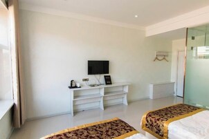 Una habitación de hotel con una cama, un televisor en un mueble, un escritorio y una puerta de vidrio que da al baño.