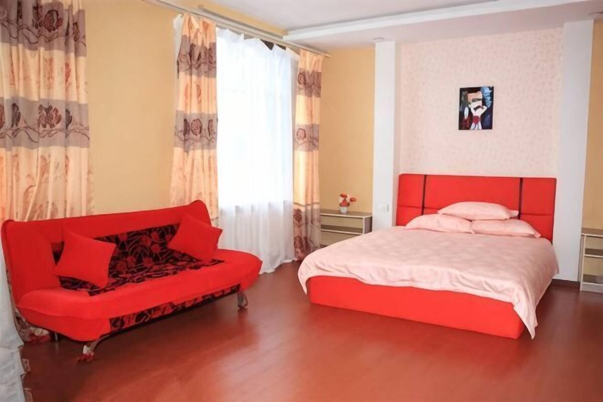 Una habitación con un sofá rojo, una cama con cabecera roja y un cartel en la pared.