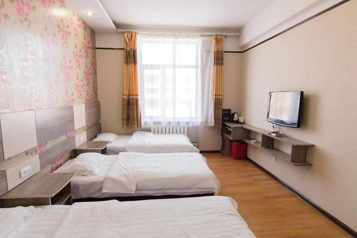 Habitación de hotel con tres camas, un televisor, una ventana con cortinas y una pared con estampado floral.