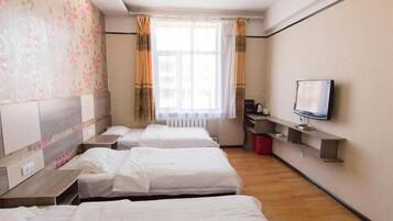 A hotel room with three beds, a television, a window with curtains, and a wall with a floral pattern.