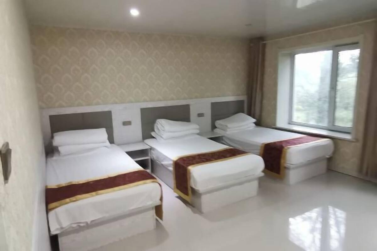 Habitación de hotel con tres camas, un ventanal grande y un papel tapiz estampado.