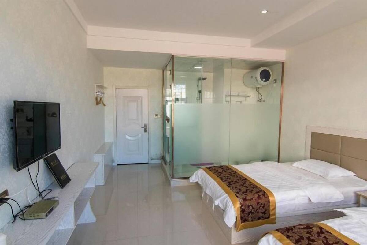 Habitación de hotel con cama, televisión, cabina de ducha de vidrio y puerta que da a otra habitación.