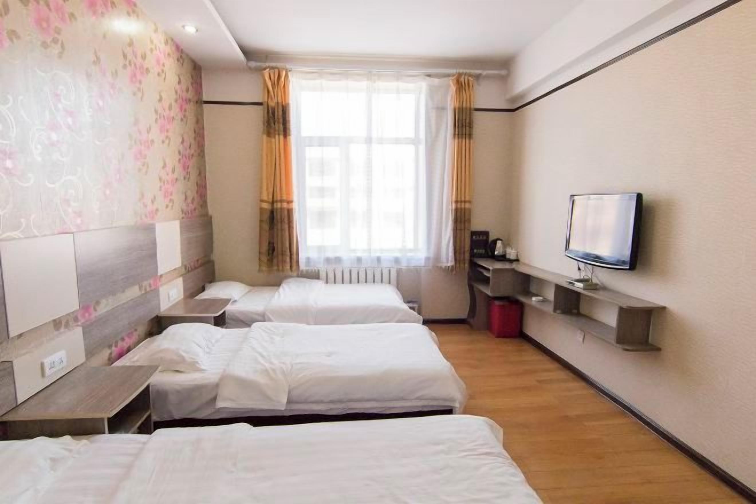 A hotel room with three single beds, a television on a shelf, and a window with curtains.