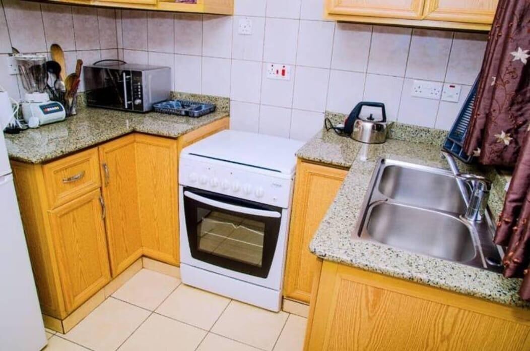 Una cocina compacta con armarios de madera, un horno blanco, un microondas, un tostador y un lavamanos.