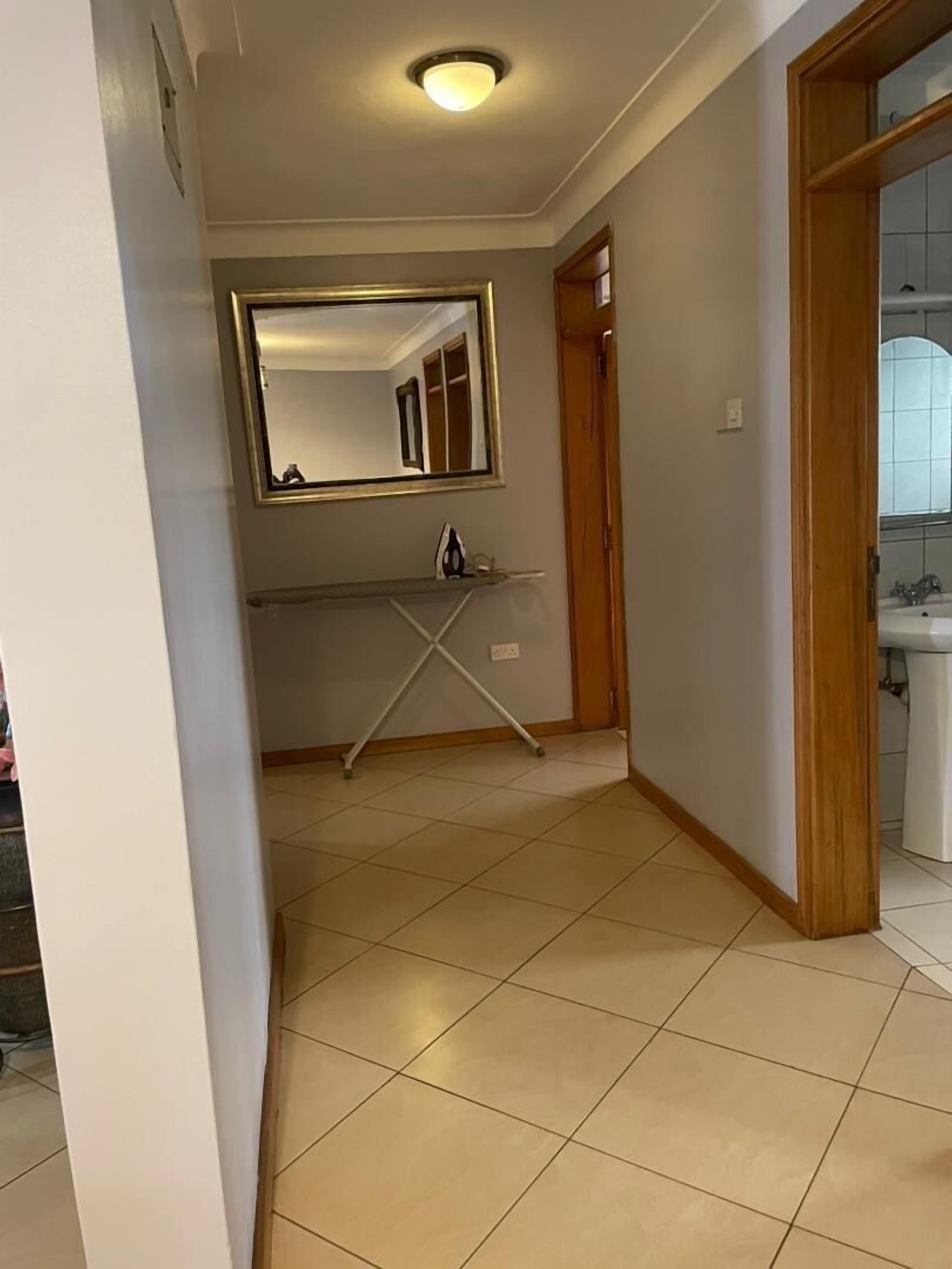 Un pasillo con piso de baldosas, un espejo en la pared y una puerta que da a un baño.