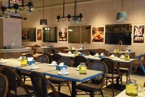 Ein Restaurantinneres mit gedeckten Tischen, Stühlen, hängenden Lampen und Wandbildern.