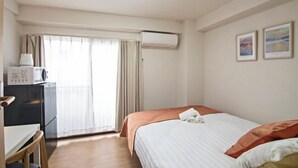 A hotel room with a bed, a desk, a chair, a window with curtains, and an air conditioning unit. - Daikoku Apartment 602 - Namba Apt3 minJR Imamiya/Daikokucho St/Veranda (Osaka)