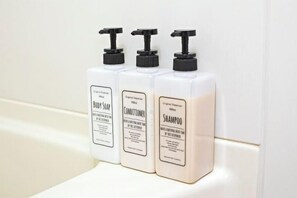 Trois bouteilles de savon pour le corps, d’après-shampoing et de shampoing, posées sur une surface blanche.
