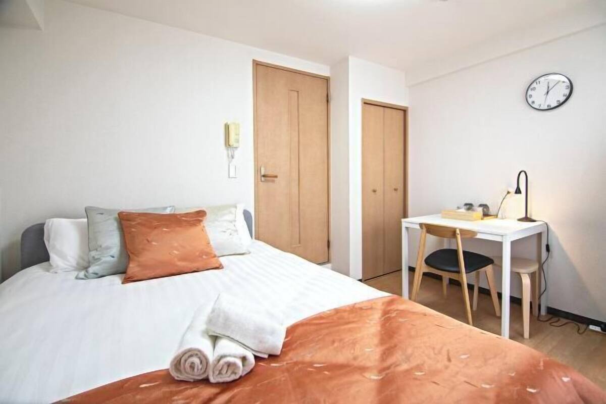 A bedroom with a bed, a desk, a chair, a clock, and a wardrobe.