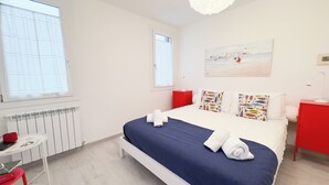 A hotel room with a bed, a red nightstand, a white desk, and a painting on the wall. - Maison De La Brodeuse by Ca-Sa Check (Chioggia)