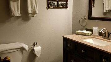 A bathroom with a toilet, sink, and mirror. There are towels hanging on a rack and a toilet paper holder.