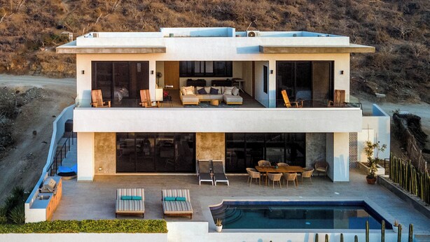 Une maison moderne à deux étages, dotée d’un grand balcon, d’un espace extérieur aménagé et d’une piscine.