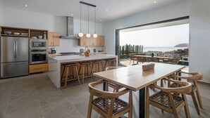 Une cuisine moderne dotée d’un îlot central, d’appareils électroménagers en acier inoxydable et offrant une vue sur l’océan.