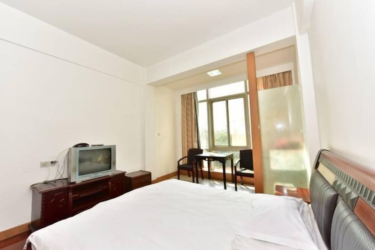 A hotel room with a bed, a television on a wooden stand, a desk with a chair, and a window with curtains.