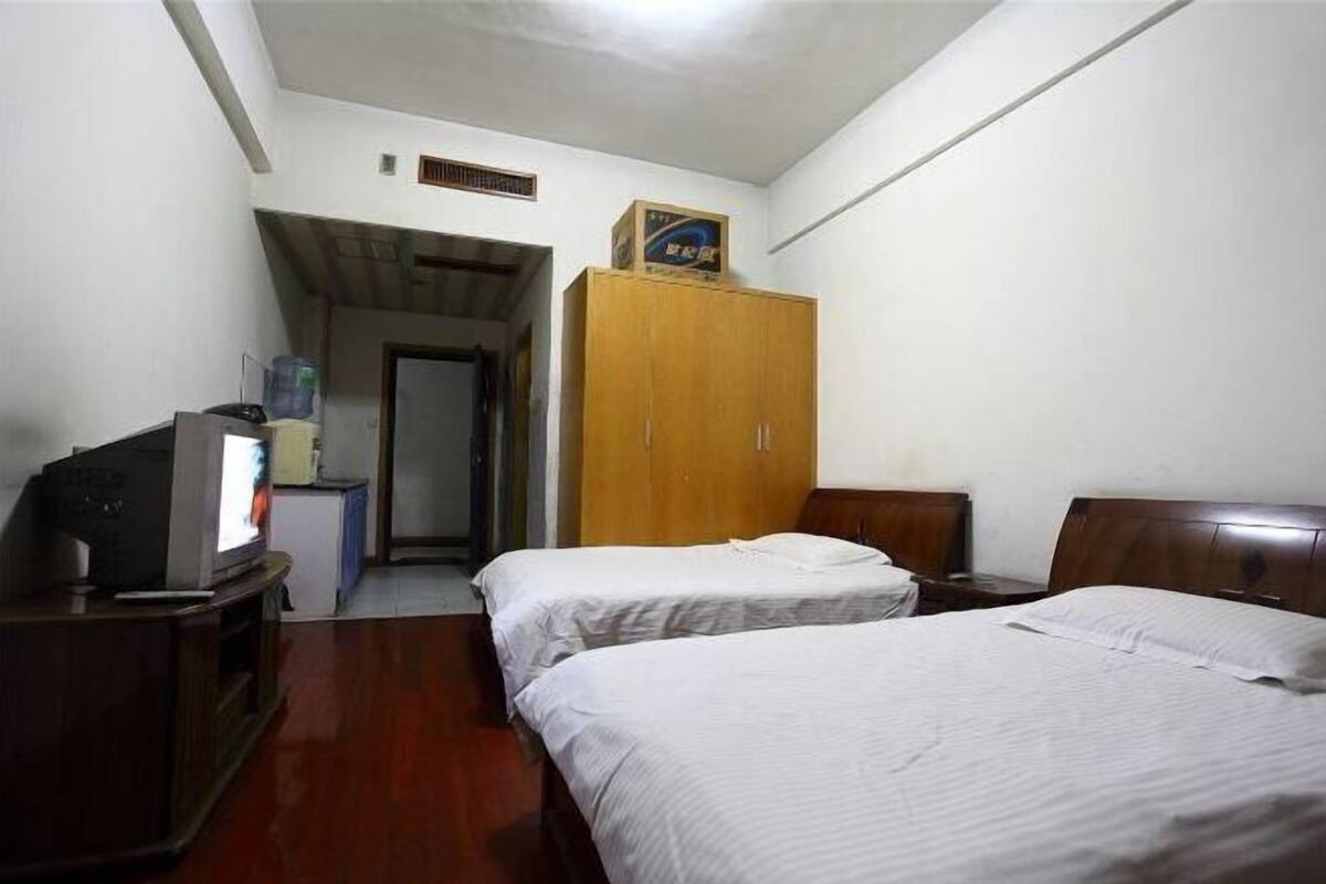 A hotel room with two single beds, a wooden wardrobe, a television on a wooden stand, and a small table.
