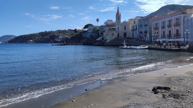 A coastal town with a prominent church, a sandy beach, and a rocky shoreline.