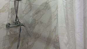 Suihkussa on sekä käsisuihkupää että kiinteä suihkupää, ja molemmat on asennettu seinään, jossa on marmorikuvioitu laattapinta.