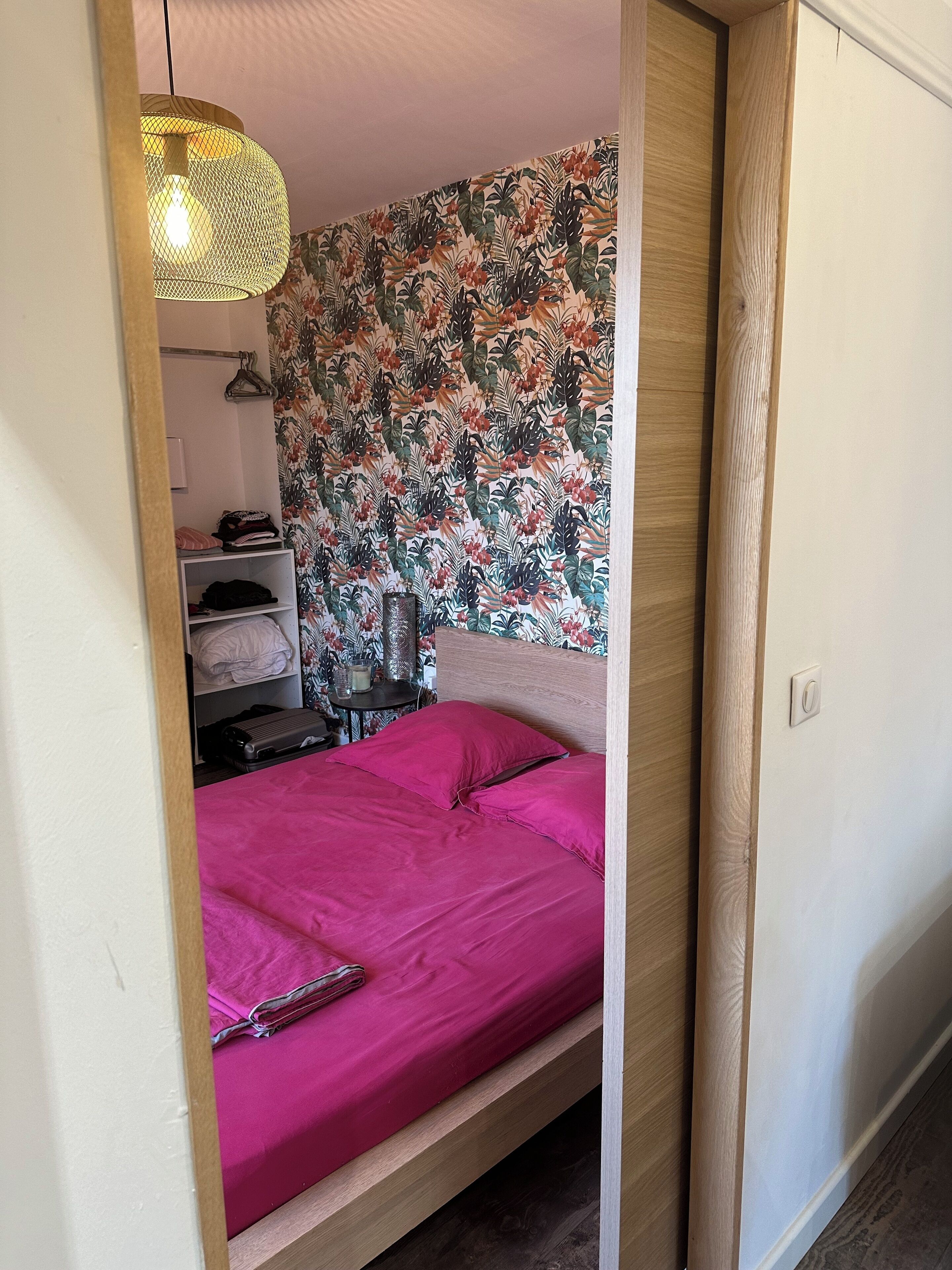 Une chambre à coucher avec un lit, un luminaire suspendu, une armoire et une étagère avec des vêtements pliés.