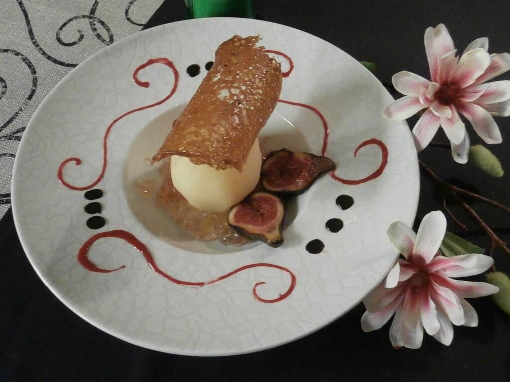 A dessert on a plate with a decorative design, accompanied by flowers.