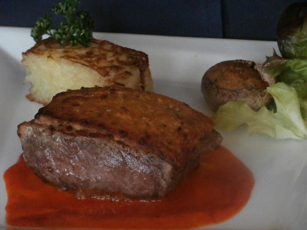 A plate with a piece of meat, a baked item, and a small round vegetable.