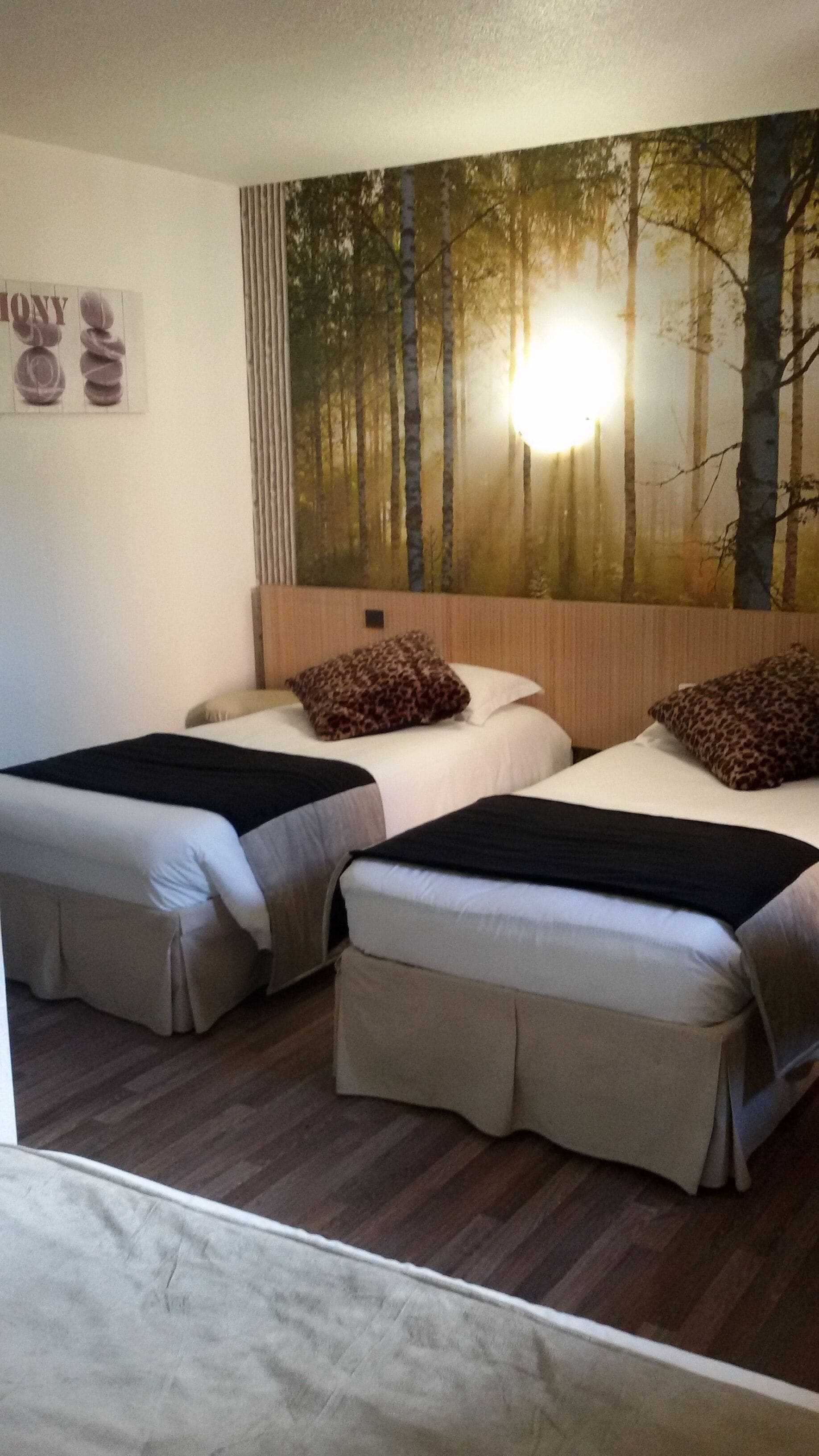 Een kamer met twee bedden, een wanddecoratie van een bos en een houten vloer.