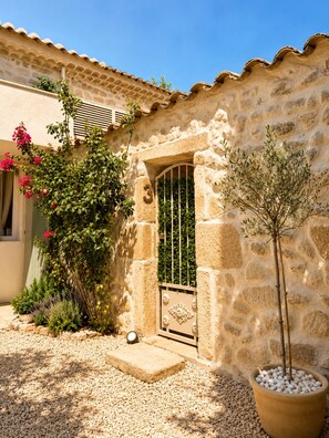 Un bâtiment en pierre avec un toit en tuiles, une porte et un arbre en pot.