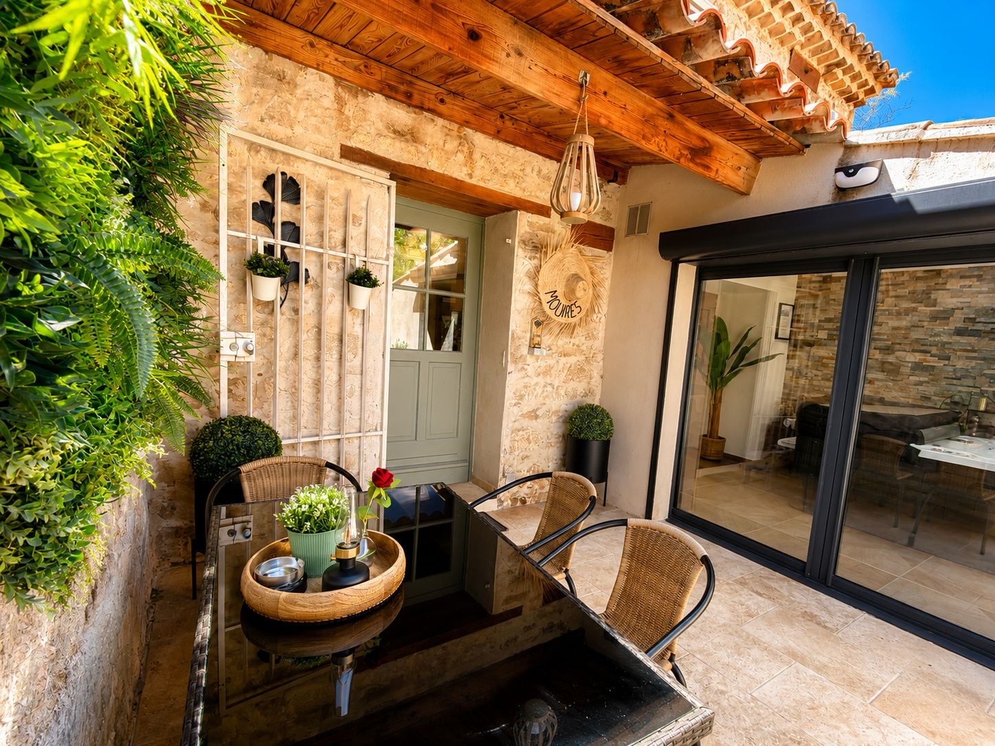 Un patio al aire libre con una mesa de madera, sillas y plantas en macetas.