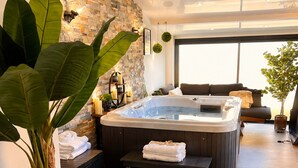 Un área de spa moderna con una pared de piedra, una bañera de hidromasaje, un banco y una planta en maceta.