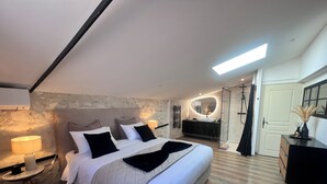Un dormitorio moderno con una cama grande, mesitas de noche, un tocador con espejo y una ducha a pie.