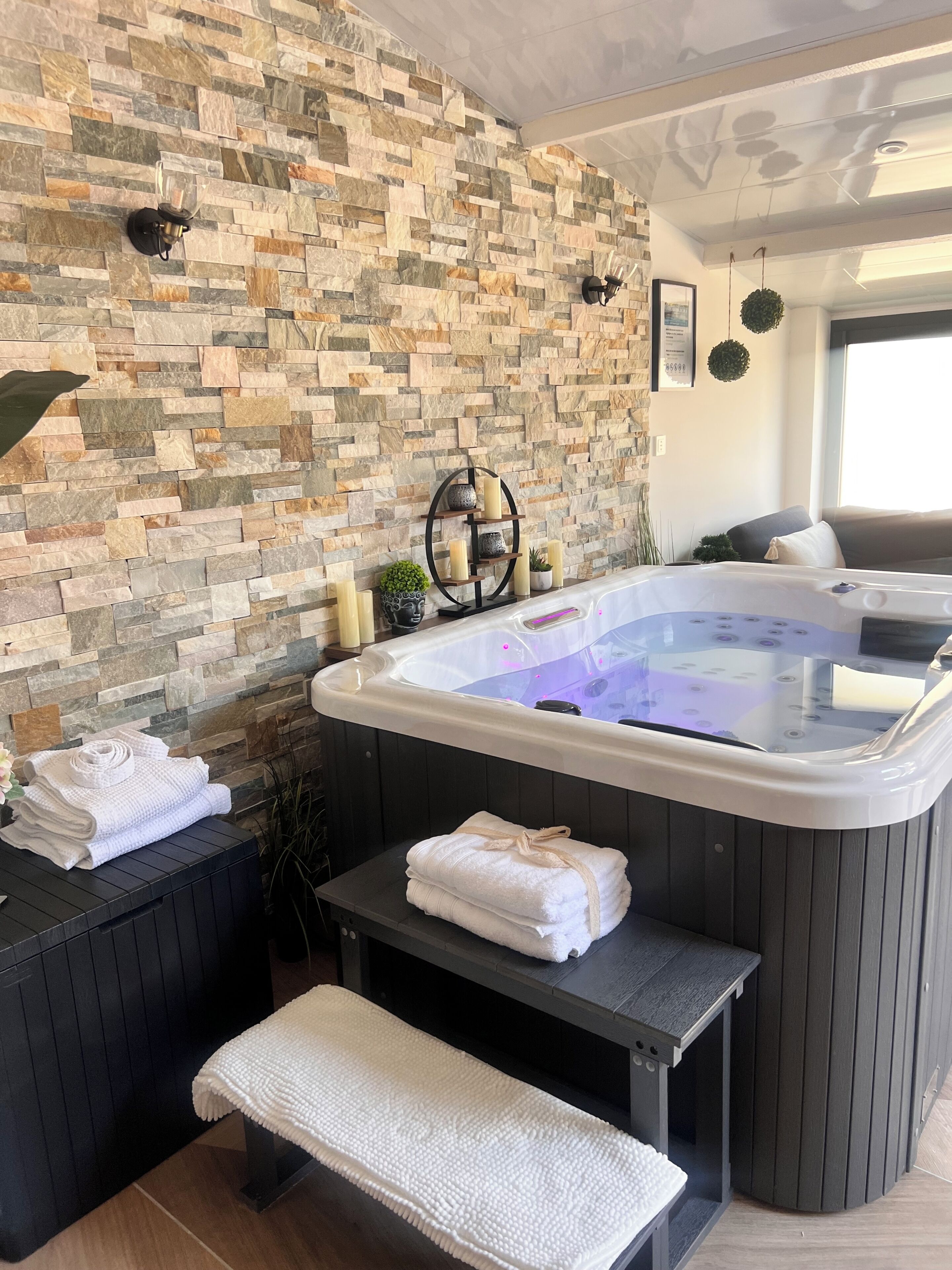 A spa room with a stone wall, a hot tub, towels, and a bench.