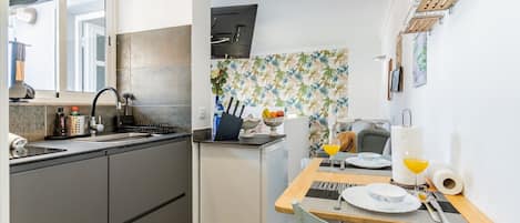 A compact kitchen with a sink, stove, and a small refrigerator. There's a dining area with a table set for two, a chair, and a vase with flowers.