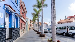 A street lined with palm trees and colorful buildings, a white van parked on the side, and a clear sky.