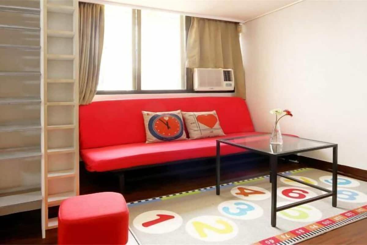 A room with a red sofa, a glass coffee table, a ladder, and a window with curtains.