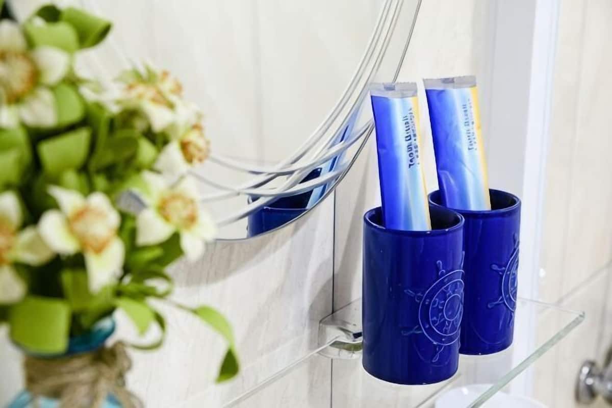 A bathroom with a blue towel rack holding two towels, a clear glass shelf with a vase of flowers, and a white tiled wall.