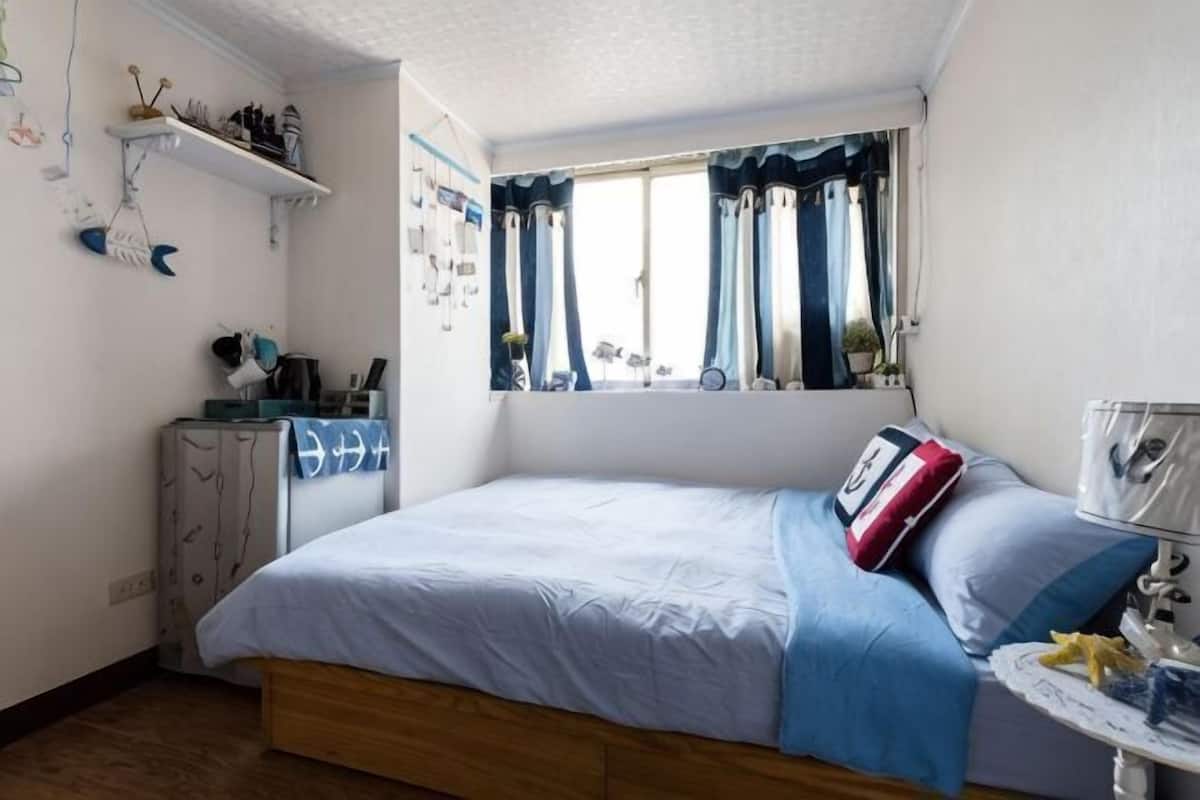 A bedroom with a bed, a window with curtains, a bedside table, and a dresser.