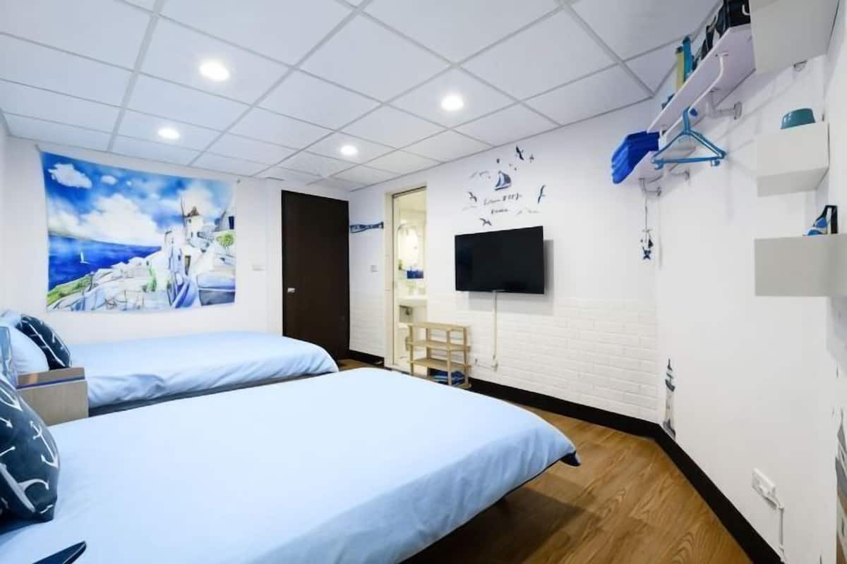 A hotel room with two beds, a TV, a painting, and a wooden floor.