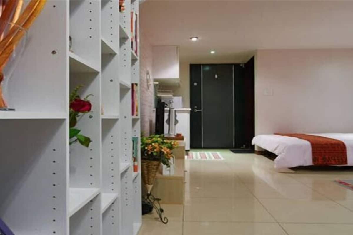A hotel room with a bed, a white shelving unit, and a door leading to a hallway.