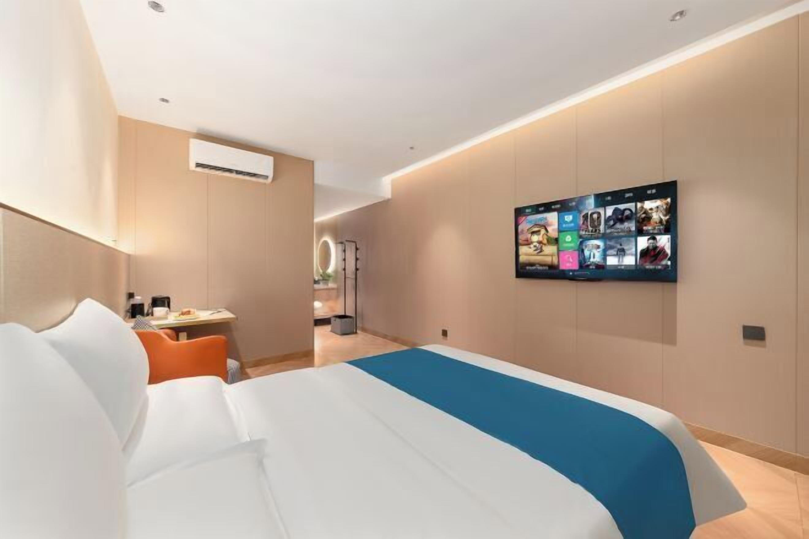 A hotel room with a bed, a desk, and a TV mounted on the wall displaying various channels.