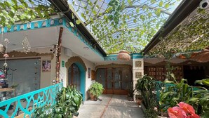 Un giardino interno con soffitto in vetro, piante in vaso e un ingresso centrale.