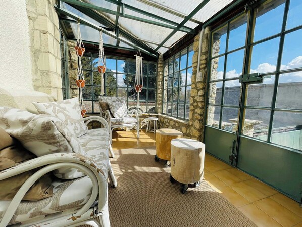 A room with a glass ceiling, stone walls, a white sofa, a patterned armchair, and a small wooden table.