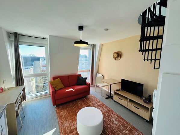 A modern living room with a red sofa, a white table, a TV, and a large window offering a city view.