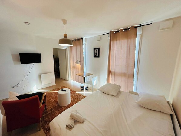 A hotel room with a bed, a desk, a chair, a TV mounted on the wall, and a bathroom visible through an open door.