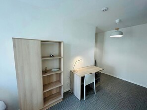 A room with a wooden bookshelf, a desk with a chair, and a pendant light. - We Live In R - Suite 203 (Reims)