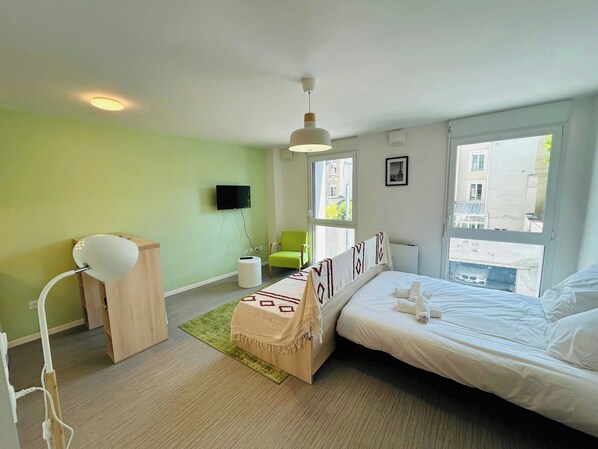 A hotel room with a bed, a desk, a chair, a TV, and a window with a view of buildings.