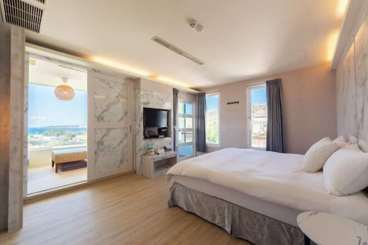 A bedroom with a large bed, a TV, a marble wall, and a balcony with a view.