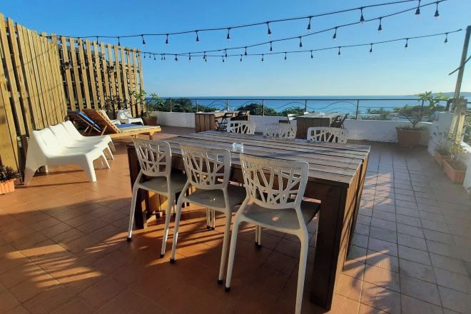 An outdoor patio with a dining table and chairs, a wooden fence, and a view of the sea.
