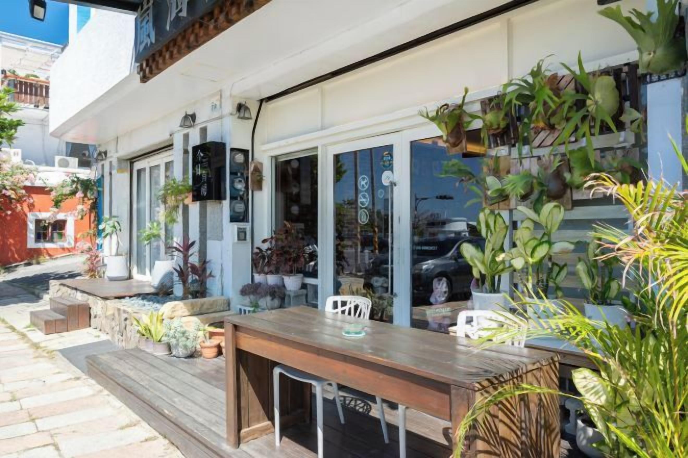 An outdoor seating area with a wooden table and chairs, surrounded by potted plants and a variety of greenery.